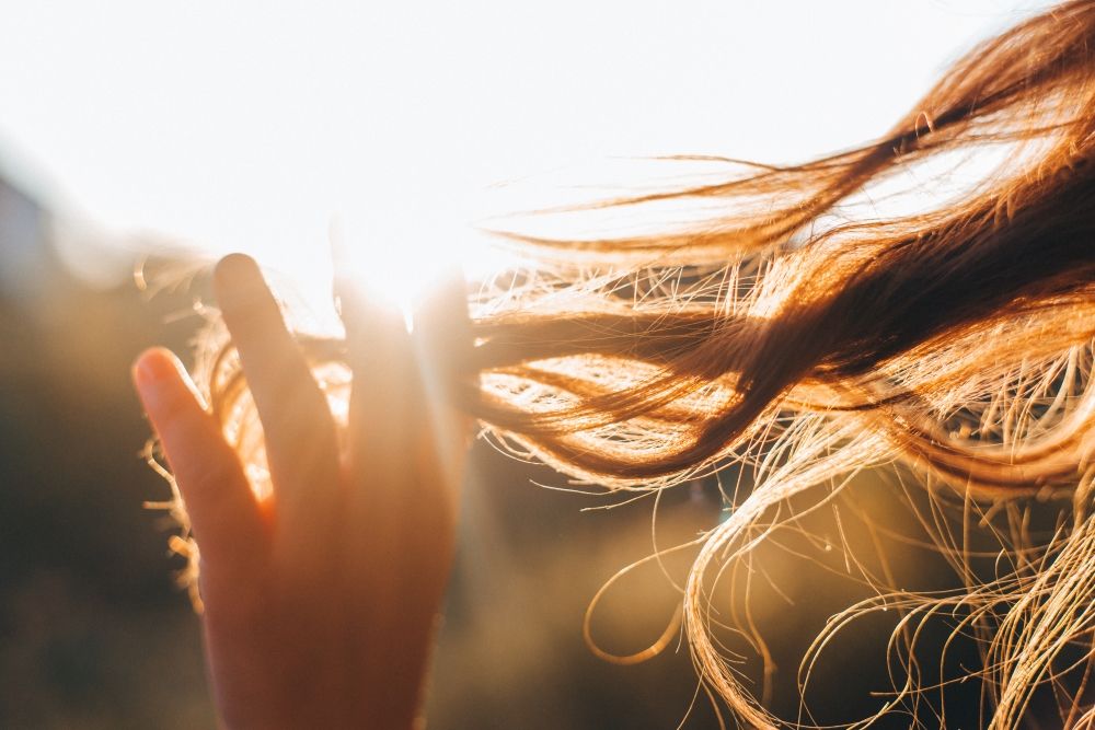 Jeune femme aux cheveux longs avec des reflets blonds devant le soleil